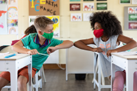 Two kids with masks touching elbows
