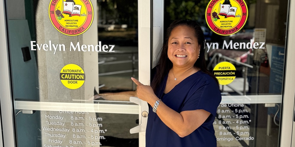 Evelyn Mendez, the newly-hired Sonoma County Registrar of Voters, stands in front of the public entrance to the Sonoma County Registrar of Voters Office where the doors now bear her name