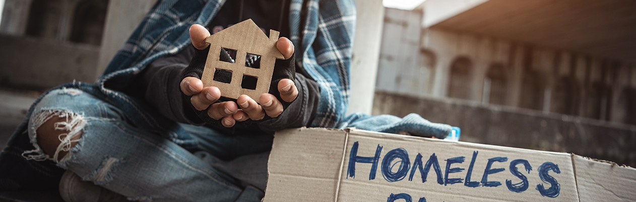 Homeless person holding cutout house with help sign